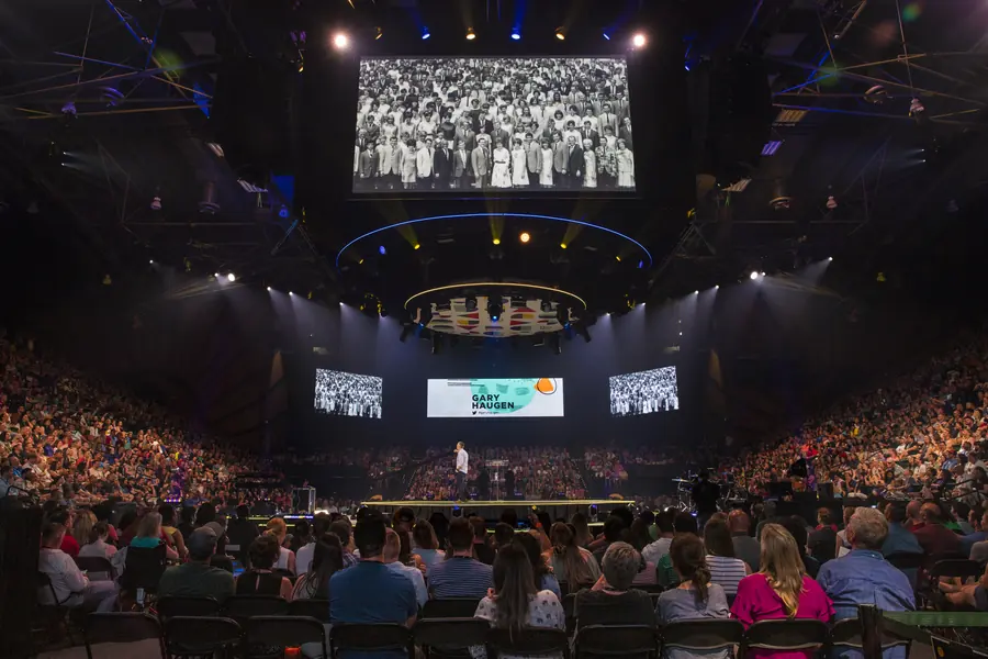 Wide arena view with stage screens during a general session