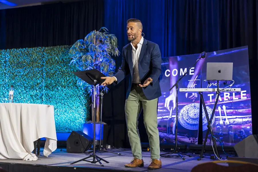 Speaker presenting on a teal and blue conference stage