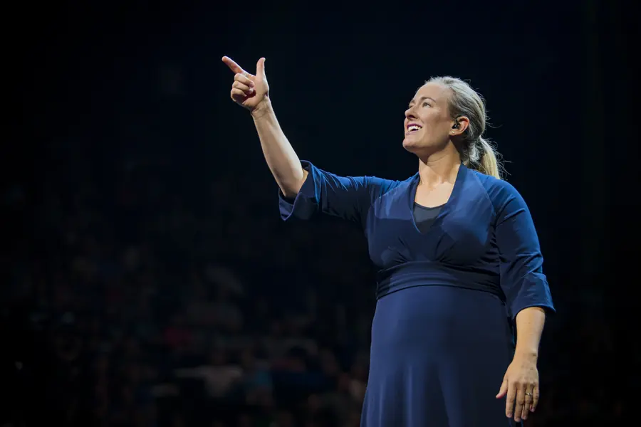 Speaker with arm raised, lit against a dark auditorium