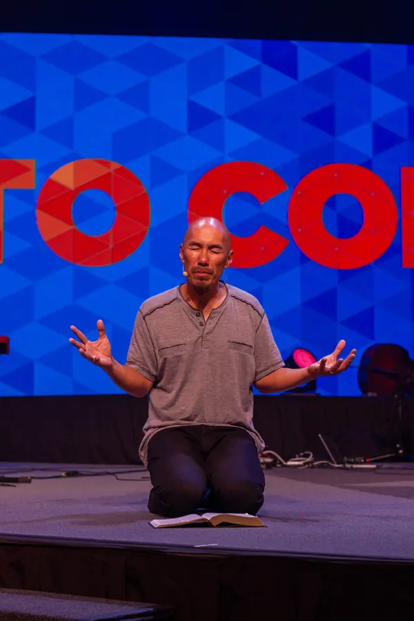 Speaker kneeling on stage before a large graphic backdrop