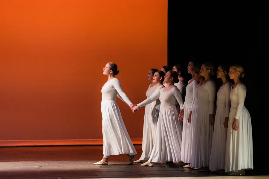 Line of dancers in cream against a split orange backdrop