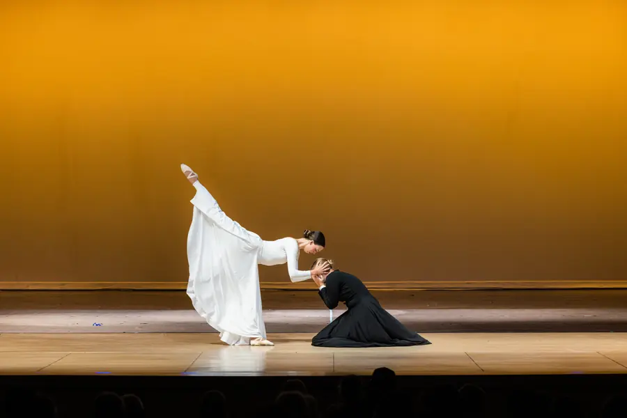 Two dancers in white and black on a golden-lit stage