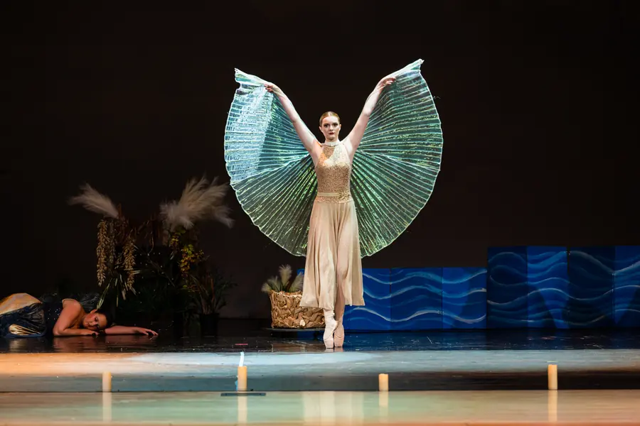 Dancer with teal fan wings raised on stage