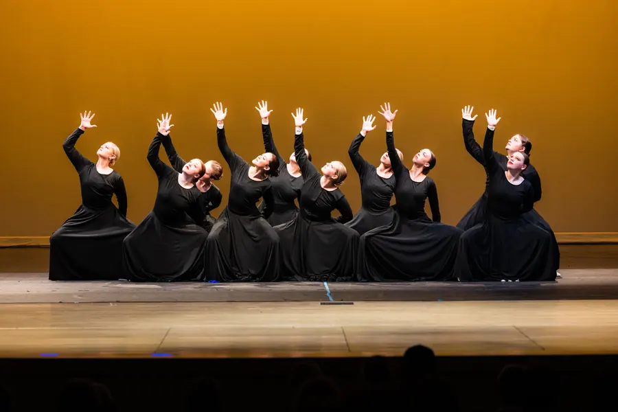 Ensemble of dancers with arms raised in unison