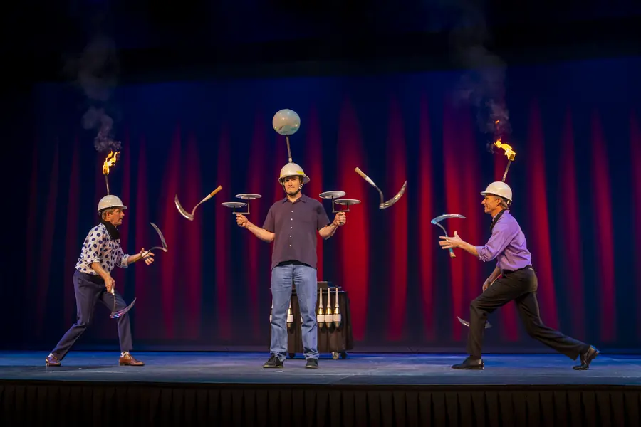Three jugglers performing with fire before a red curtain