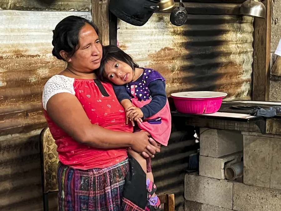 Mother holding her daughter inside their home, Guatemala