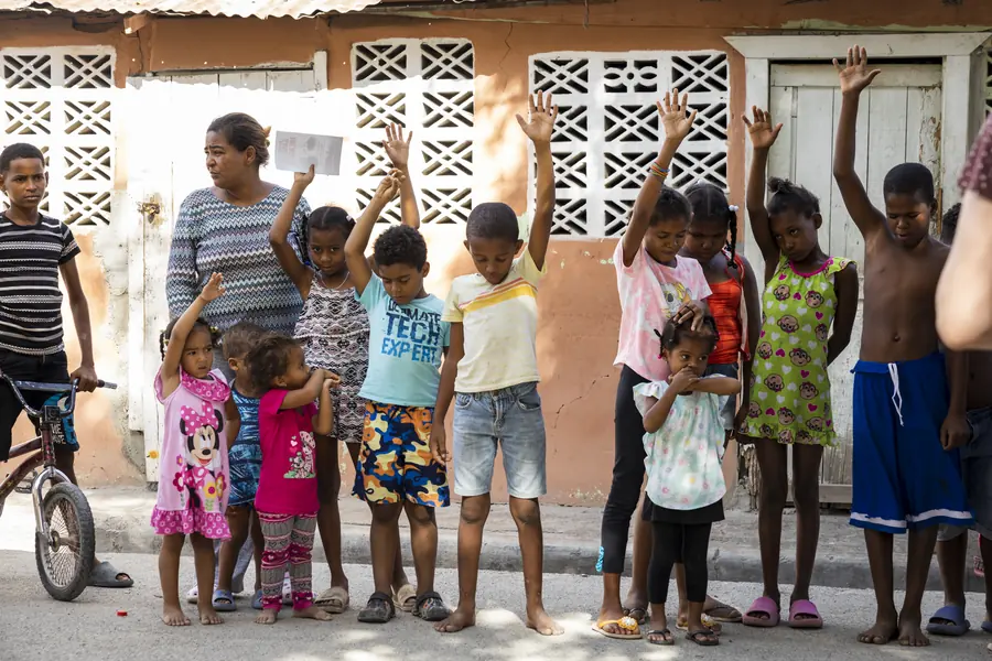 Children with hands raised outside brightly painted homes